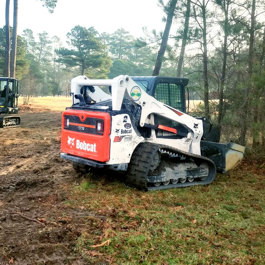 Bobcat compact track loader with a mulching head on a cleared field edged by pines