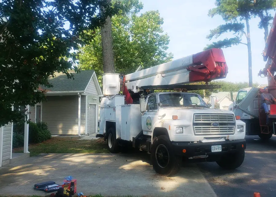 White bucket truck with its boom raised, parked in a residential driveway